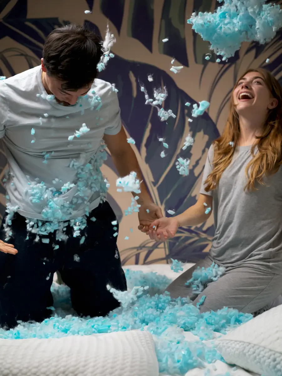 Lifestyle photograph of a couple playing with cross-cut memory foam from a bedding brand’s pillow, demonstrating the product’s safety and eco-friendliness